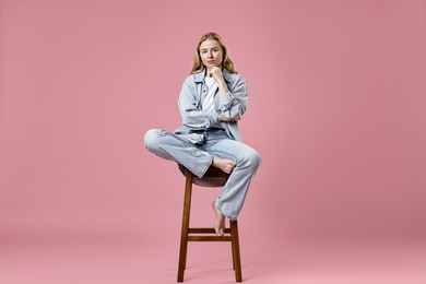 Photo of Beautiful young woman in stylish jeans sitting on stool against pink background