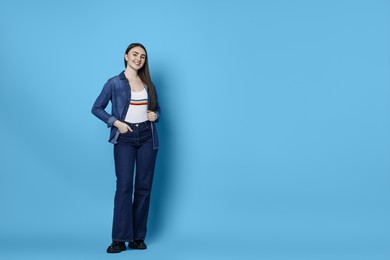 Photo of Smiling woman in stylish jeans on light blue background. Space for text