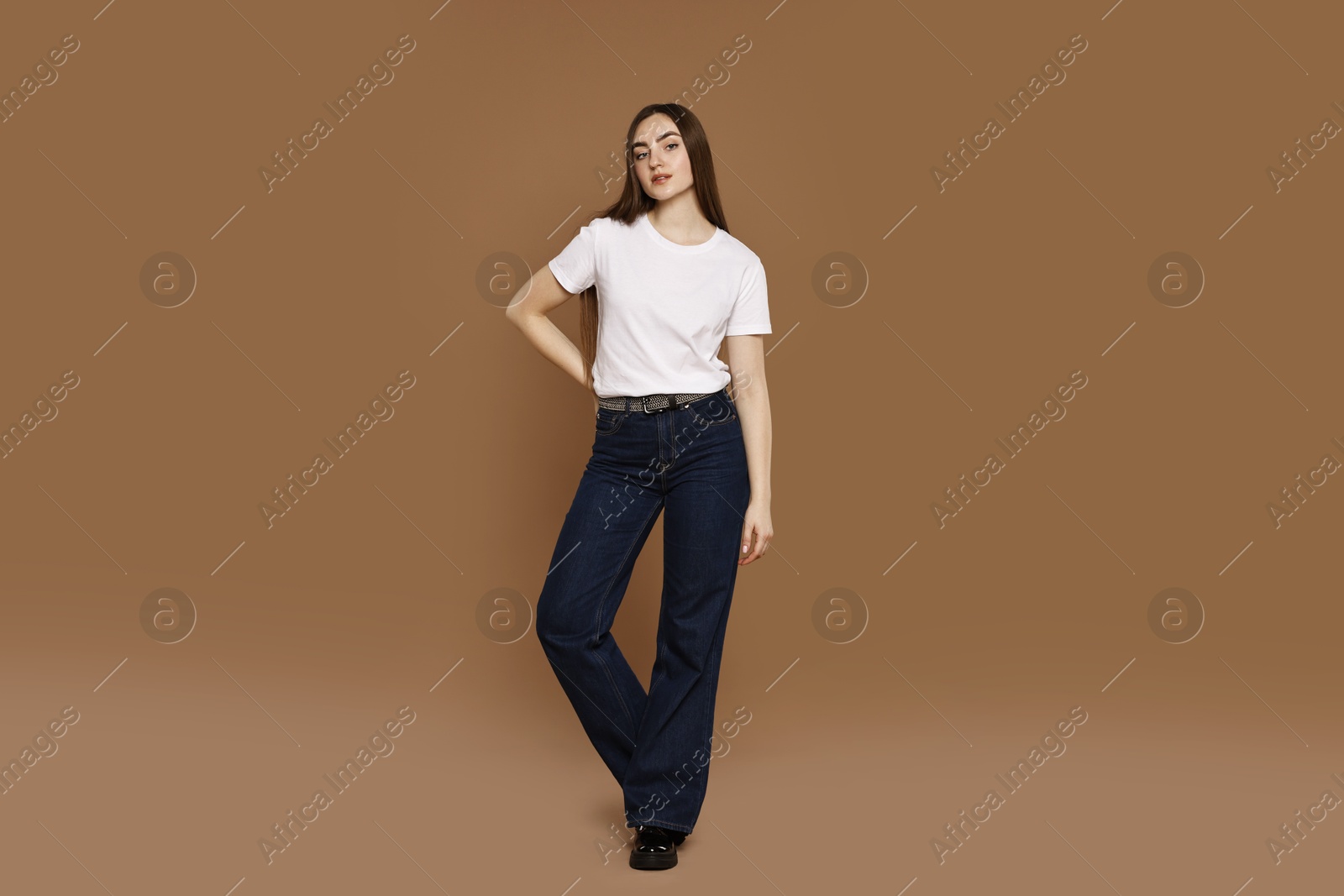 Photo of Beautiful young woman in stylish jeans on brown background