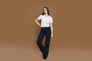 Photo of Beautiful young woman in stylish jeans on brown background