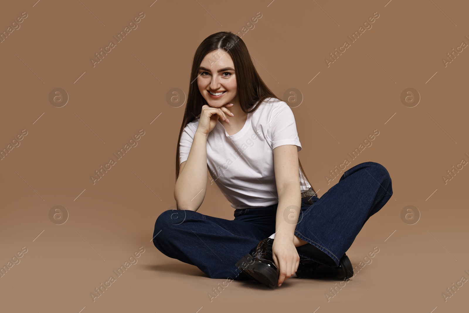 Photo of Smiling woman in stylish jeans on brown background