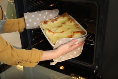 Photo of Woman taking baking dish with tasty lasagna out of oven, closeup