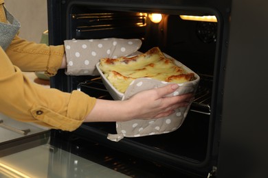 Photo of Woman taking baking dish with tasty lasagna out of oven, closeup