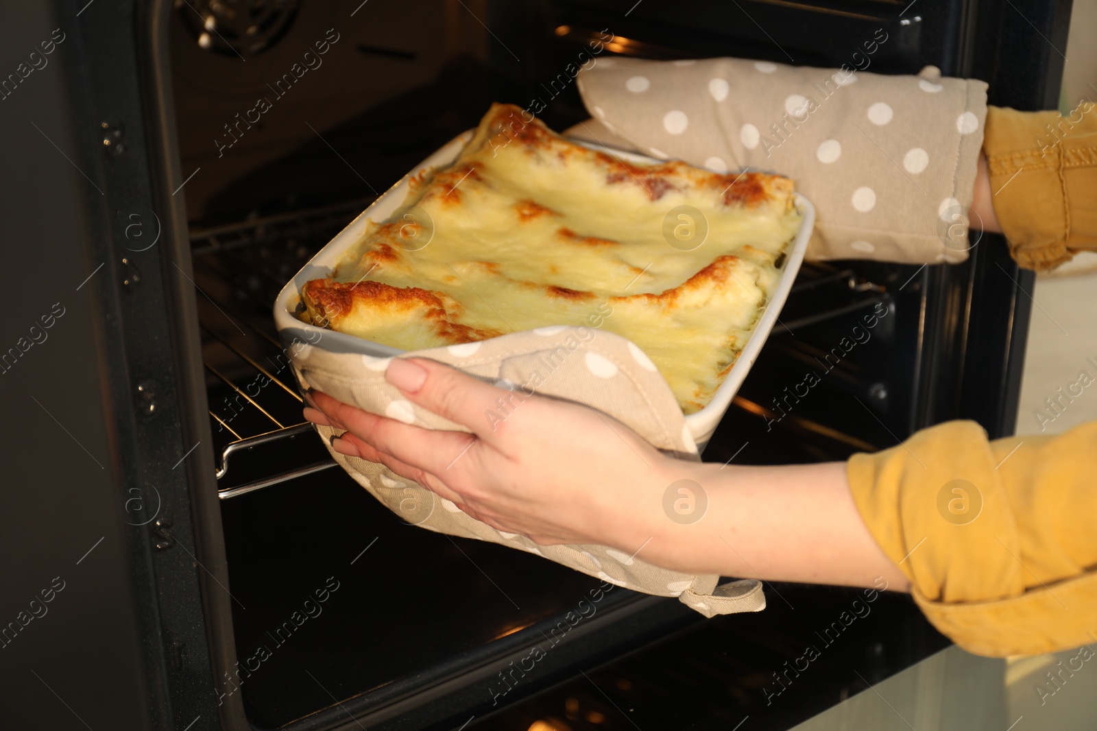 Photo of Woman taking baking dish with tasty lasagna out of oven, closeup