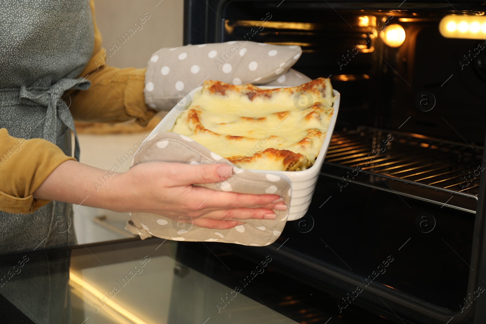 Photo of Woman taking baking dish with tasty lasagna out of oven, closeup