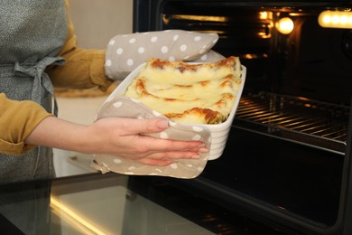 Photo of Woman taking baking dish with tasty lasagna out of oven, closeup