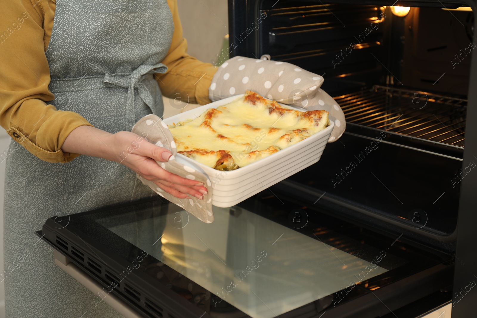 Photo of Woman taking baking dish with tasty lasagna out of oven, closeup