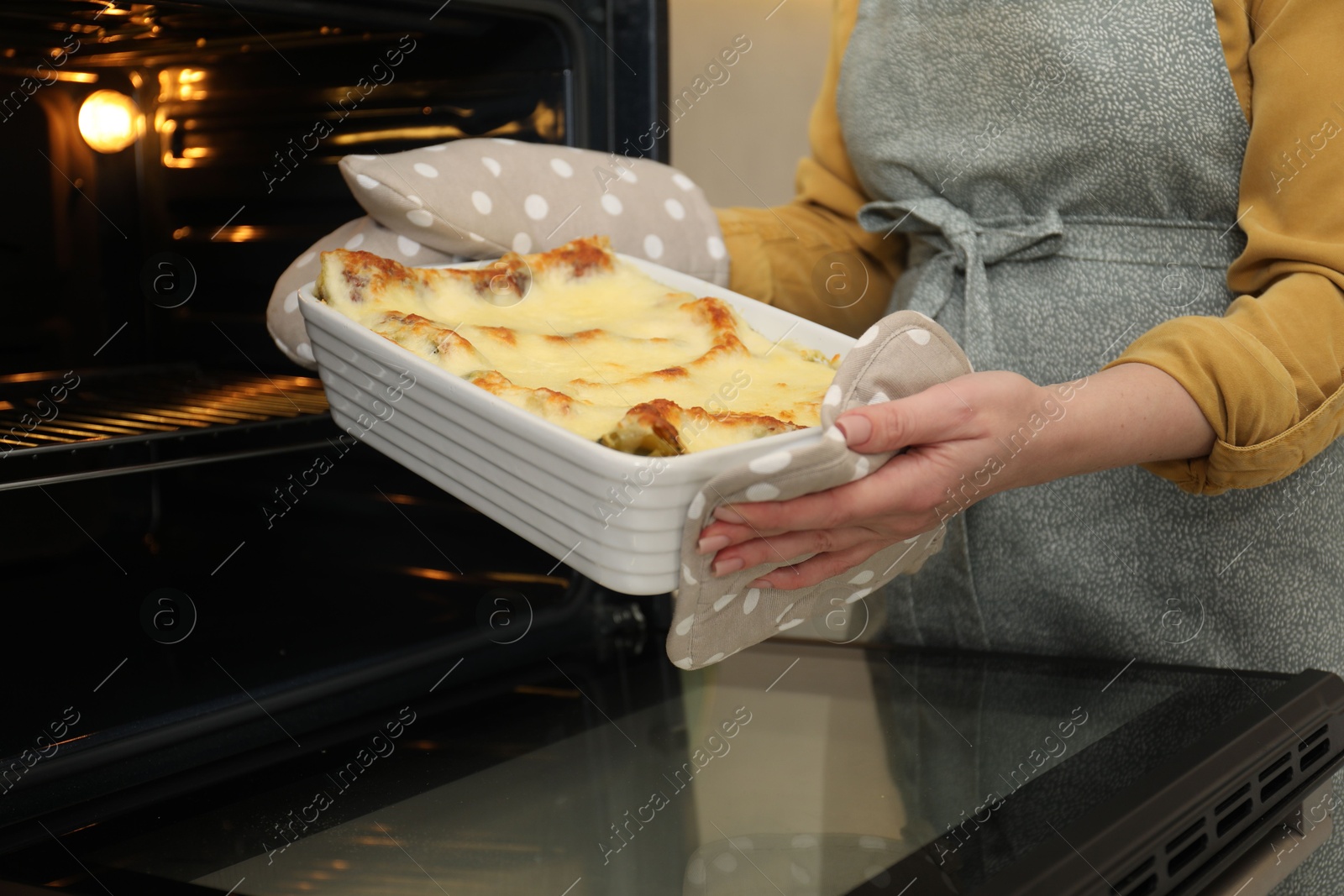 Photo of Woman taking baking dish with tasty lasagna out of oven, closeup