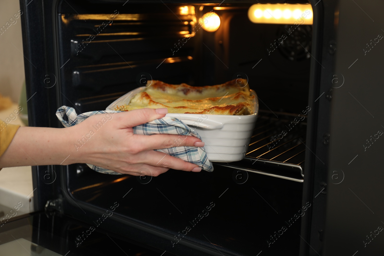 Photo of Woman taking baking dish with tasty lasagna out of oven, closeup