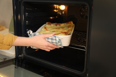 Photo of Woman taking baking dish with tasty lasagna out of oven, closeup