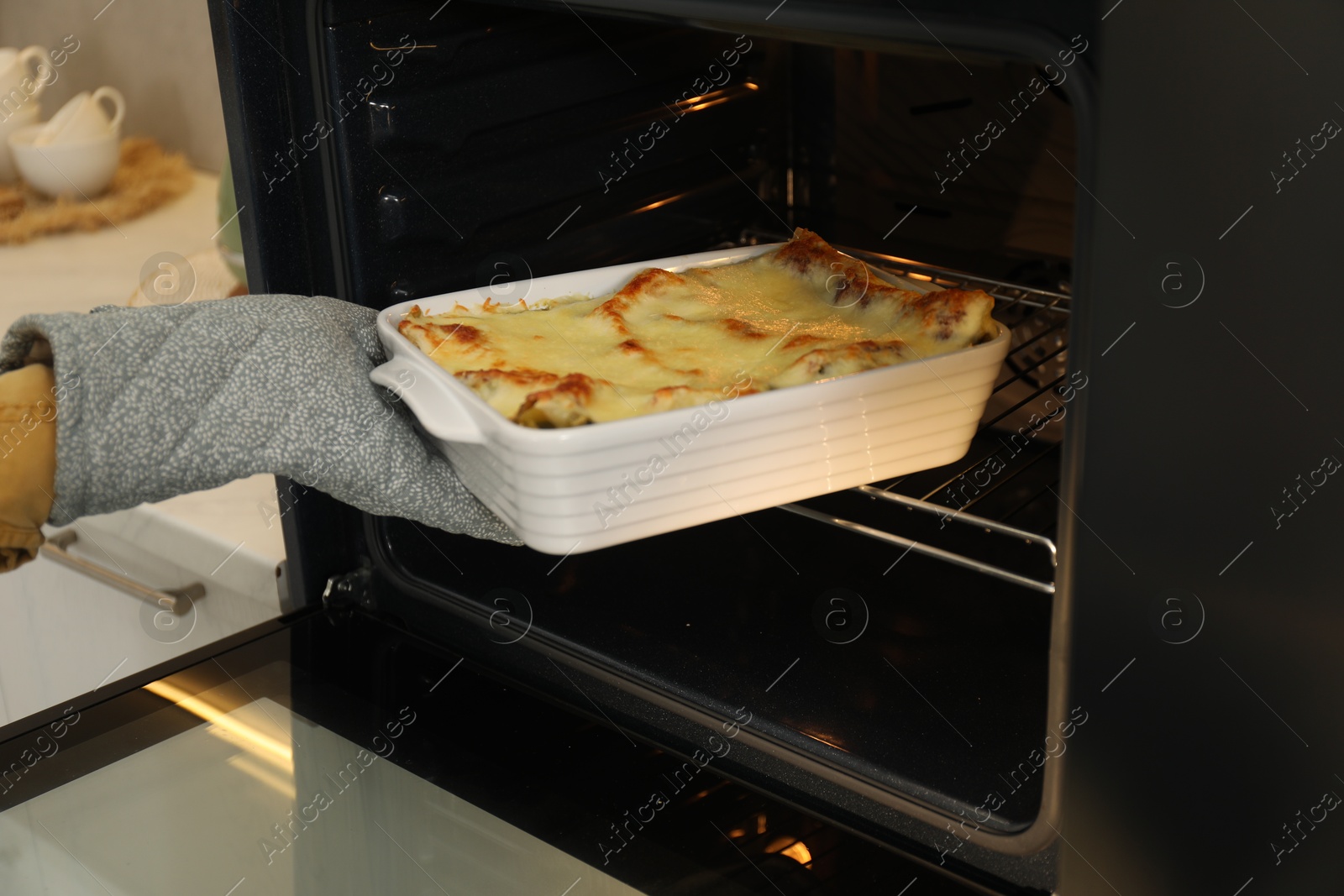 Photo of Woman taking baking dish with tasty lasagna out of oven, closeup