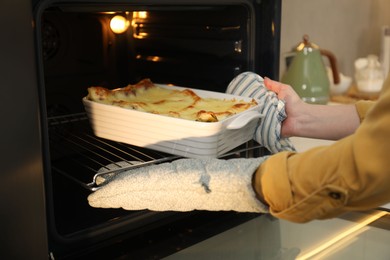 Photo of Woman taking baking dish with tasty lasagna out of oven in kitchen, closeup