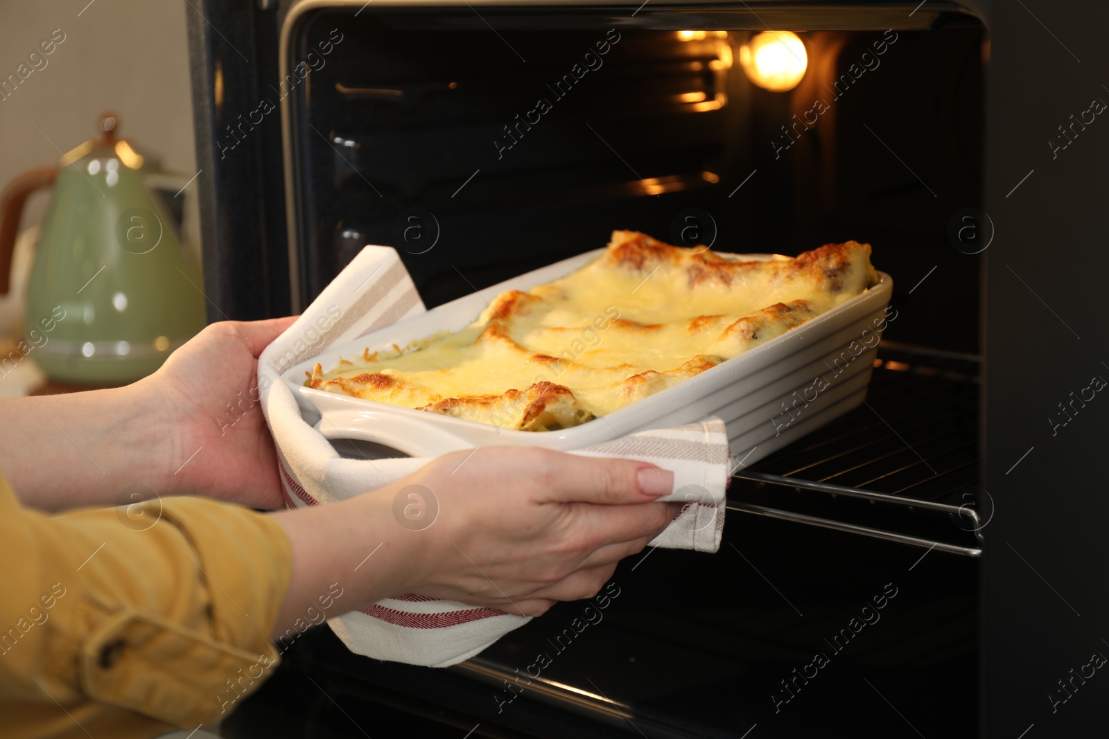 Photo of Woman taking baking dish with tasty lasagna out of oven in kitchen, closeup