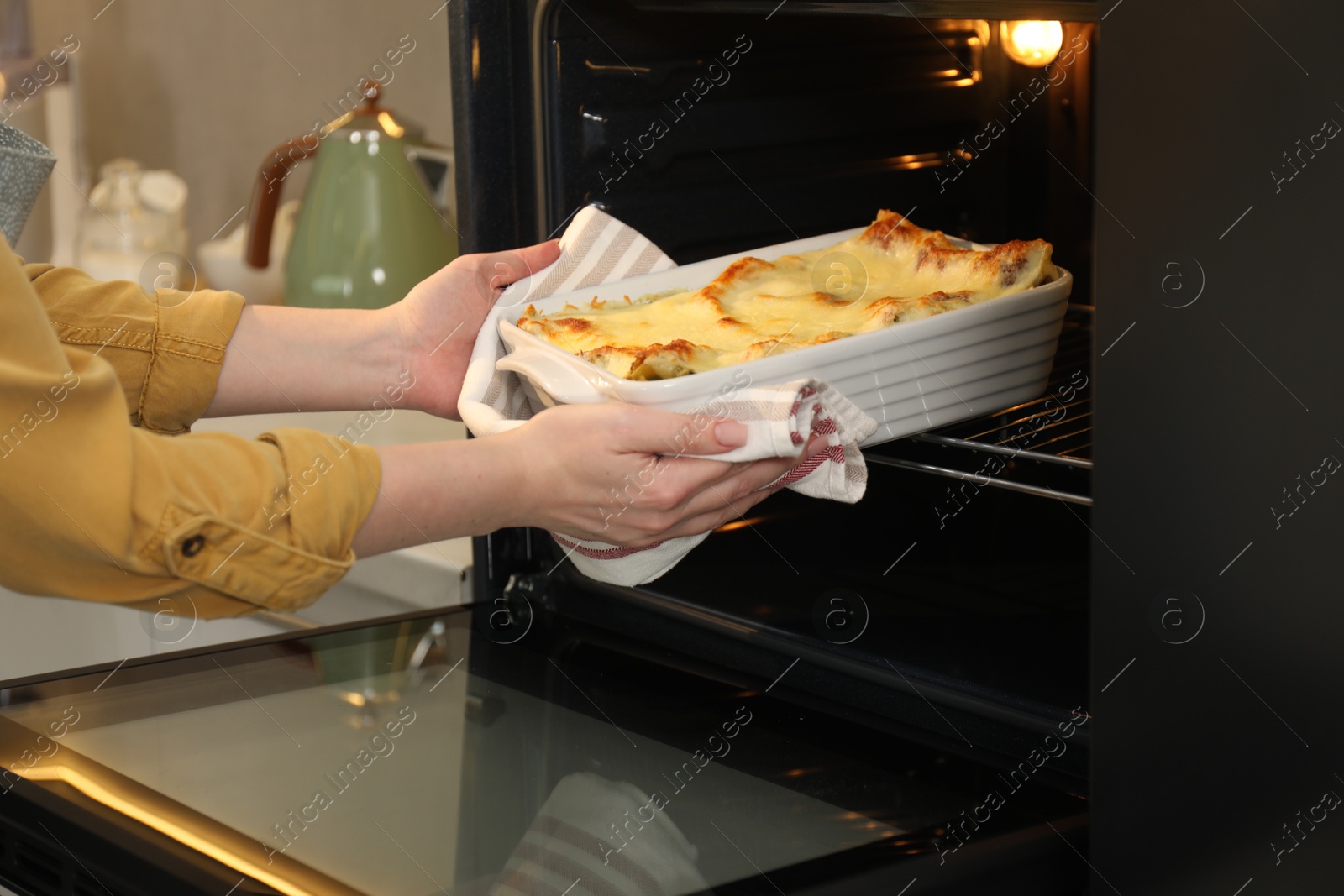 Photo of Woman taking baking dish with tasty lasagna out of oven in kitchen, closeup