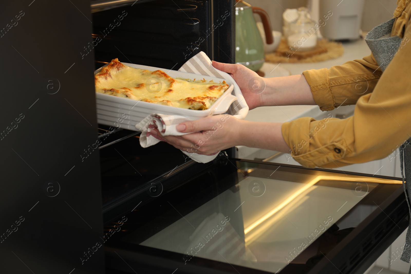 Photo of Woman taking baking dish with tasty lasagna out of oven in kitchen, closeup