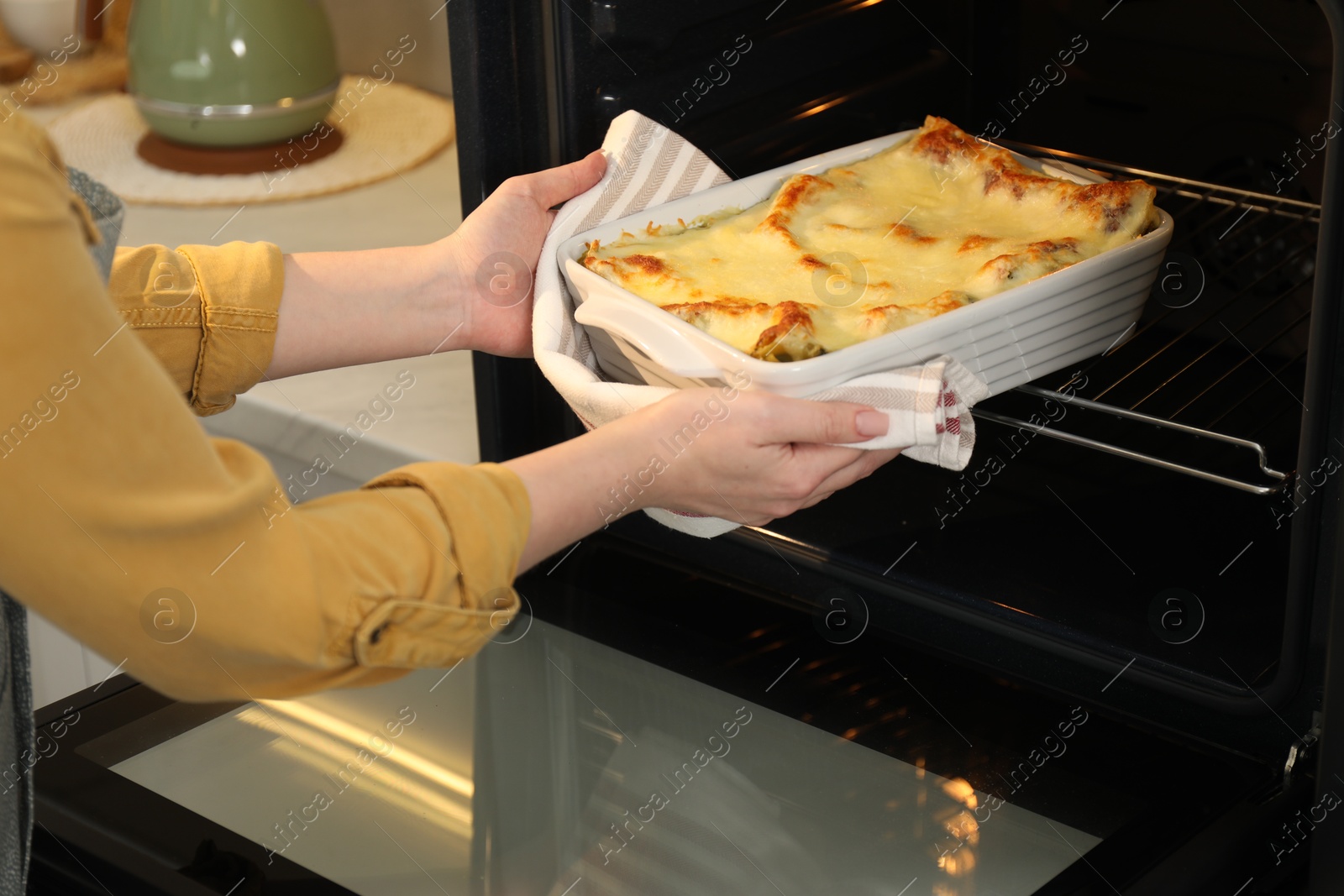 Photo of Woman taking baking dish with tasty lasagna out of oven in kitchen, closeup