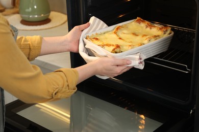 Photo of Woman taking baking dish with tasty lasagna out of oven in kitchen, closeup