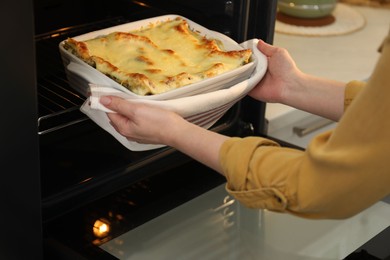 Photo of Woman taking baking dish with tasty lasagna out of oven in kitchen, closeup