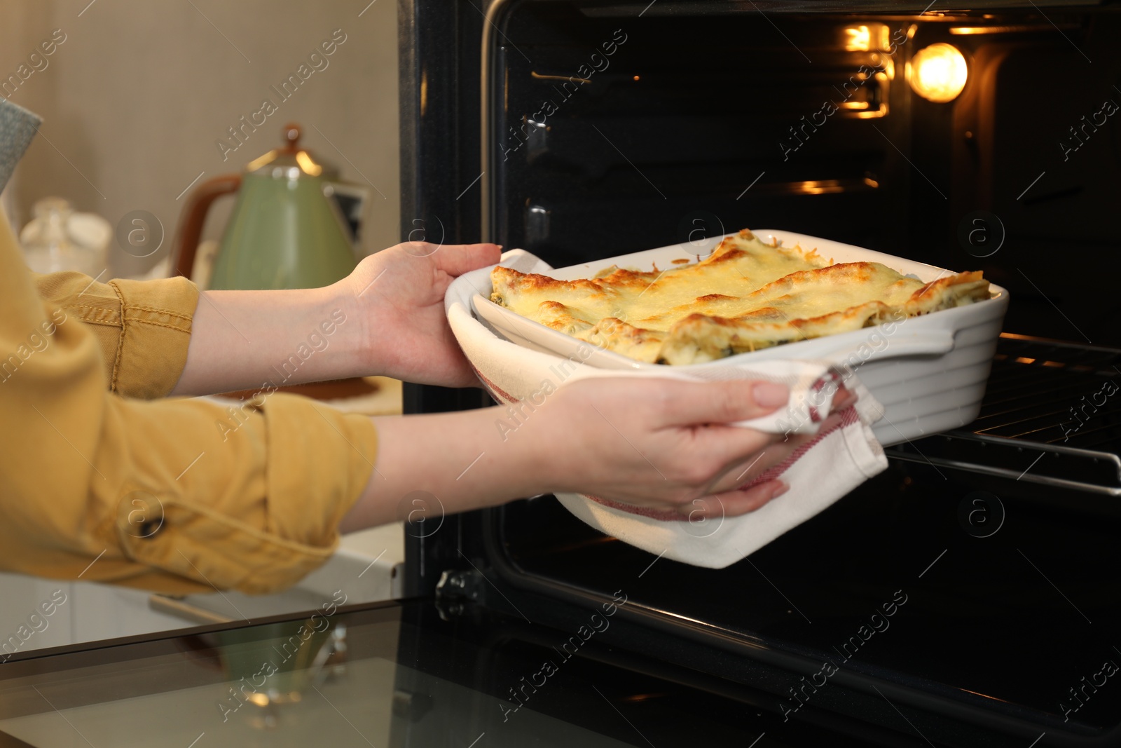 Photo of Woman taking baking dish with tasty lasagna out of oven in kitchen, closeup