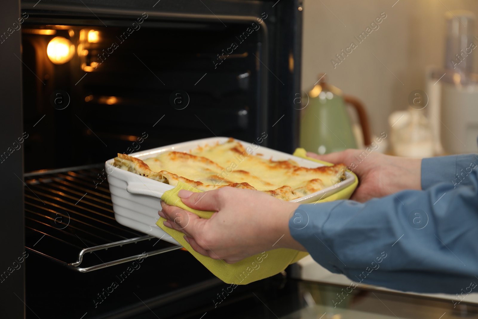 Photo of Woman taking baking dish with tasty lasagna out of oven in kitchen, closeup