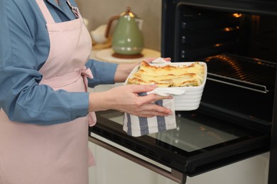 Photo of Woman holding baking dish with tasty lasagna near oven indoors, closeup