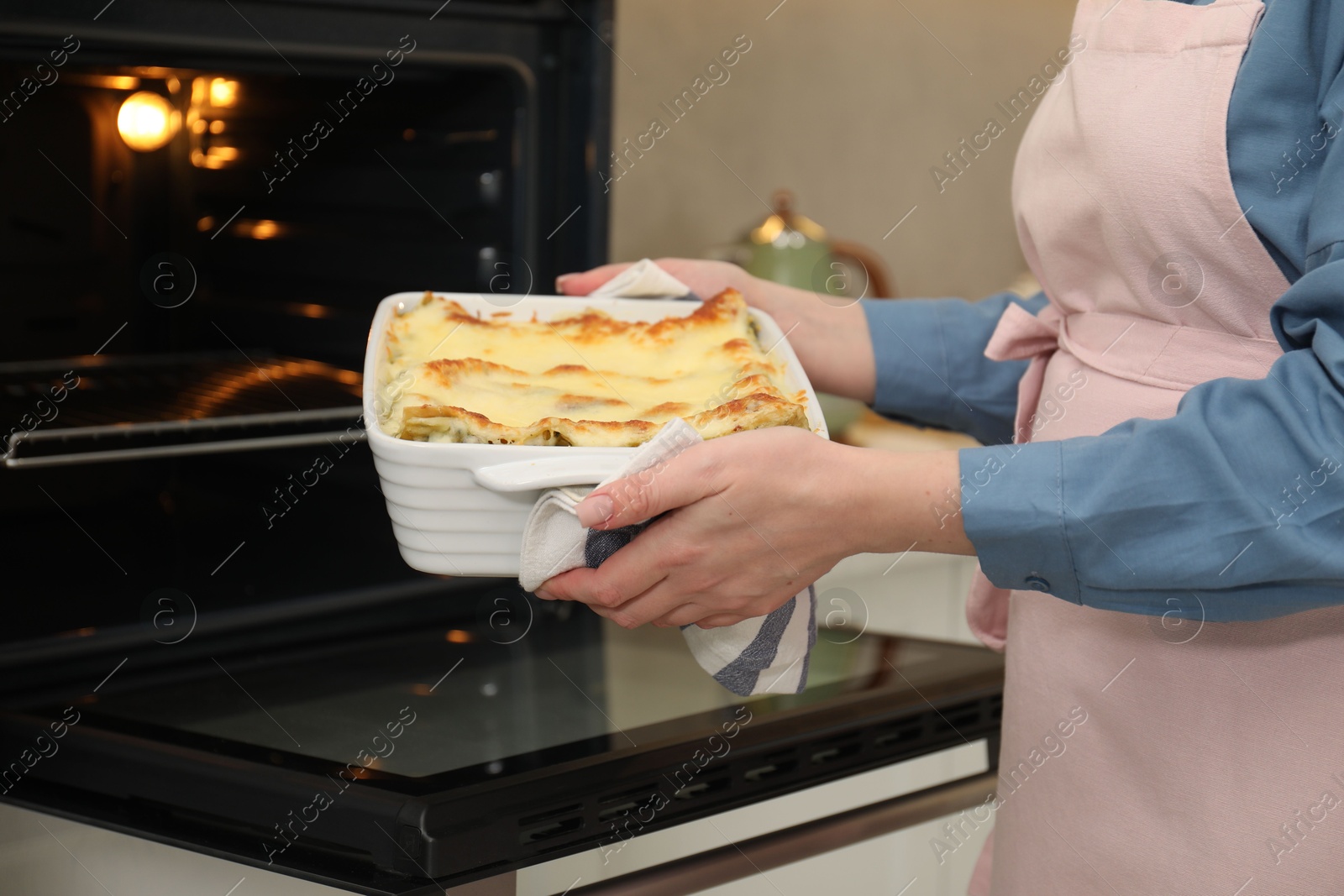 Photo of Woman holding baking dish with tasty lasagna near oven indoors, closeup