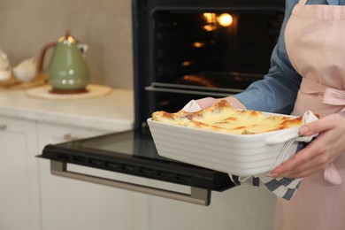 Photo of Woman holding baking dish with tasty lasagna near oven indoors, closeup