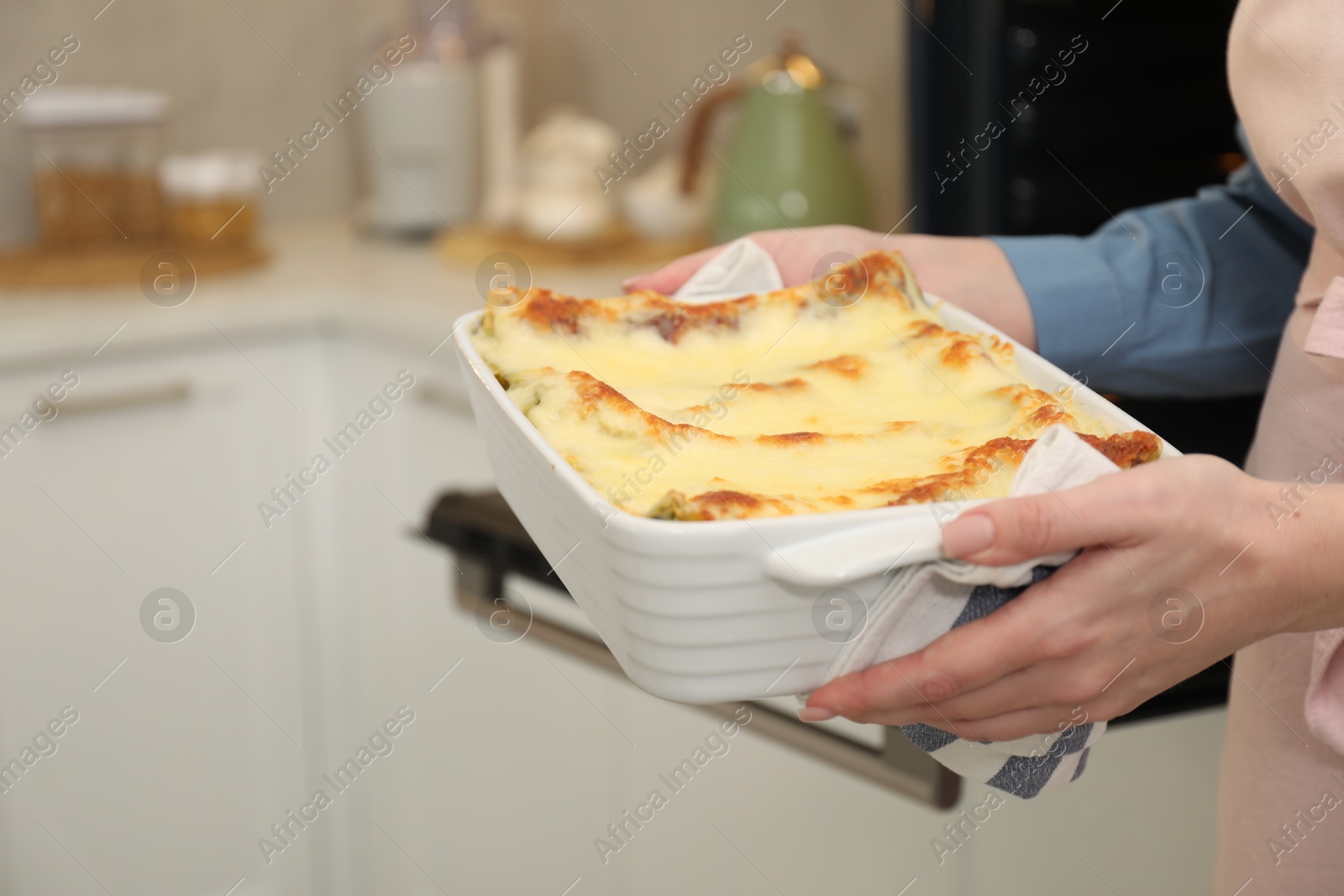 Photo of Woman holding baking dish with tasty lasagna in kitchen, closeup. Space for text