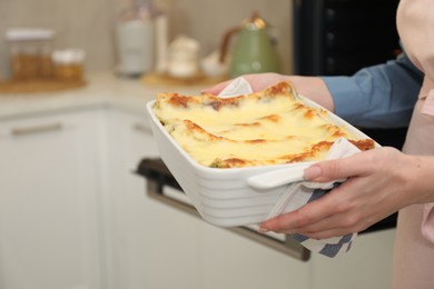 Photo of Woman holding baking dish with tasty lasagna in kitchen, closeup. Space for text