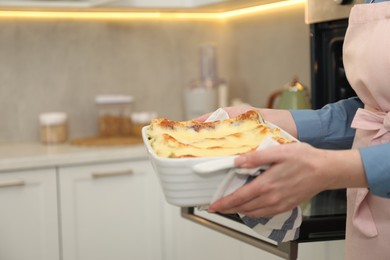 Photo of Woman holding baking dish with tasty lasagna in kitchen, closeup. Space for text