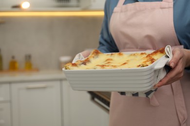 Photo of Woman holding baking dish with tasty lasagna in kitchen, closeup. Space for text