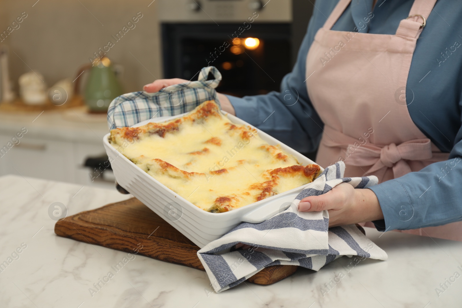 Photo of Woman holding baking dish with tasty lasagna at white marble table in kitchen, closeup