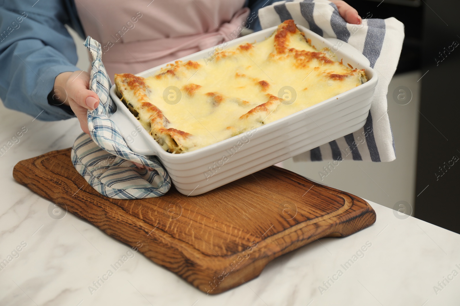 Photo of Woman holding baking dish with tasty lasagna at white marble table indoors, closeup