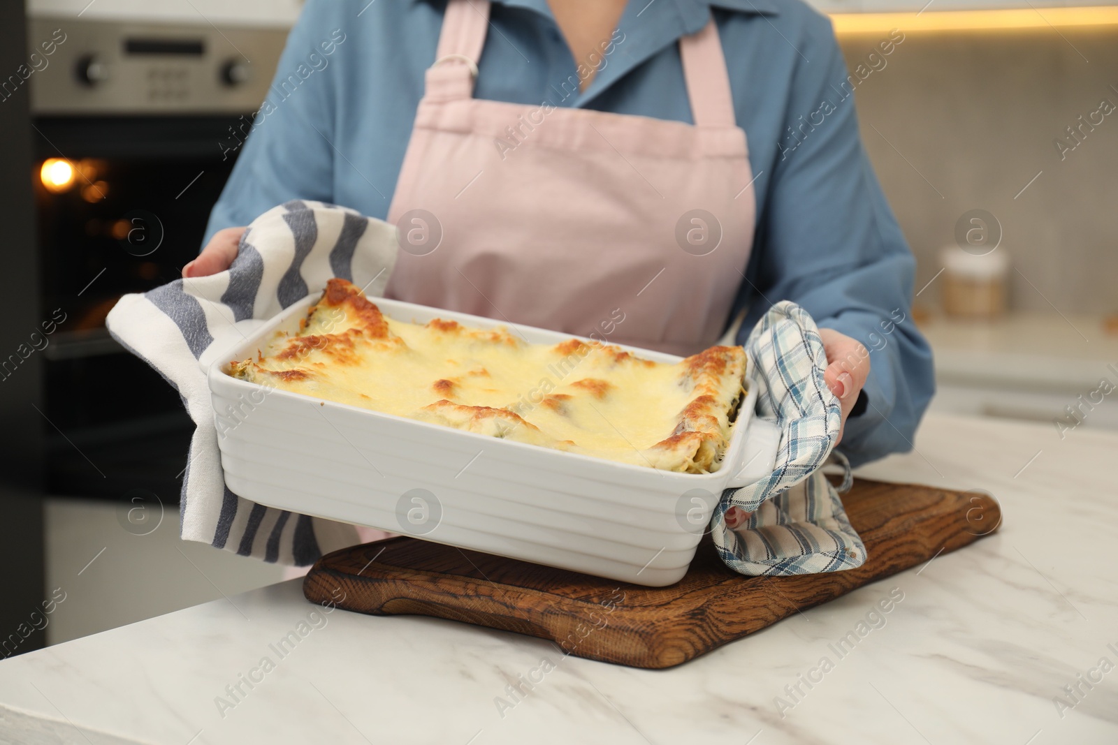 Photo of Woman holding baking dish with tasty lasagna at white marble table indoors, closeup