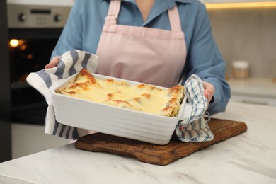 Photo of Woman holding baking dish with tasty lasagna at white marble table indoors, closeup