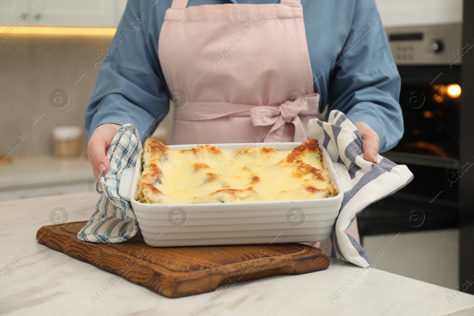 Photo of Woman holding baking dish with tasty lasagna at white marble table indoors, closeup