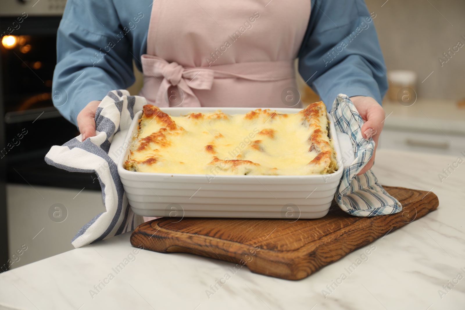 Photo of Woman holding baking dish with tasty lasagna at white marble table indoors, closeup