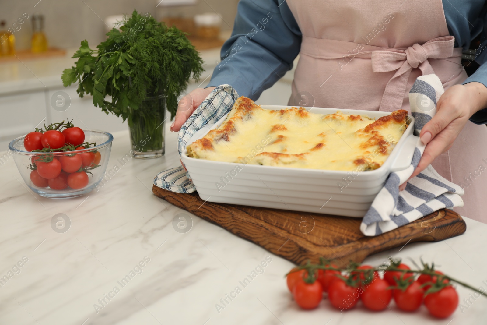 Photo of Woman putting baking dish with tasty lasagna onto white marble table indoors, closeup