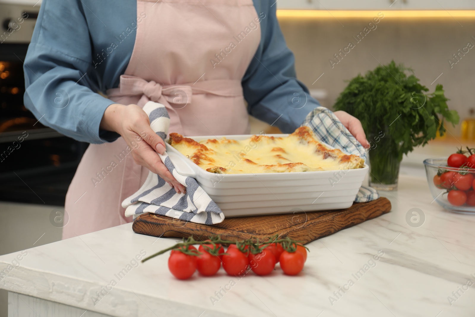 Photo of Woman putting baking dish with tasty lasagna onto white marble table indoors, closeup