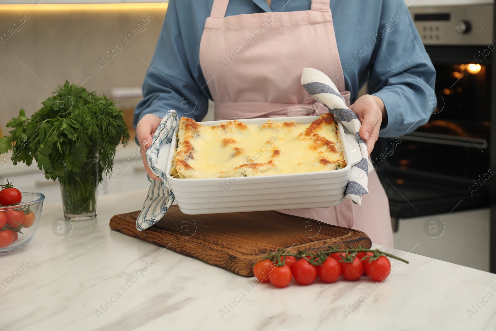 Photo of Woman putting baking dish with tasty lasagna onto white marble table indoors, closeup