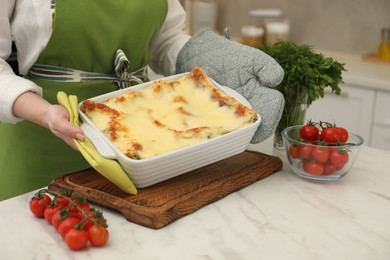 Photo of Woman putting baking dish with tasty lasagna onto white marble table indoors, closeup