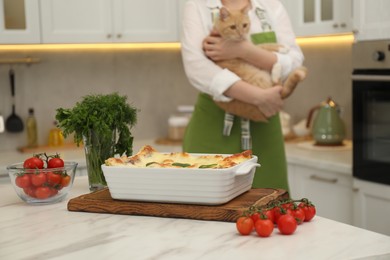 Photo of Delicious spinach lasagna on white marble table and woman with cat in kitchen, selective focus