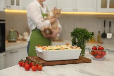 Photo of Delicious spinach lasagna on white marble table and woman with cat in kitchen, selective focus