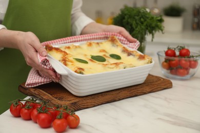 Photo of Woman putting baking dish with tasty spinach lasagna onto white marble table indoors, closeup