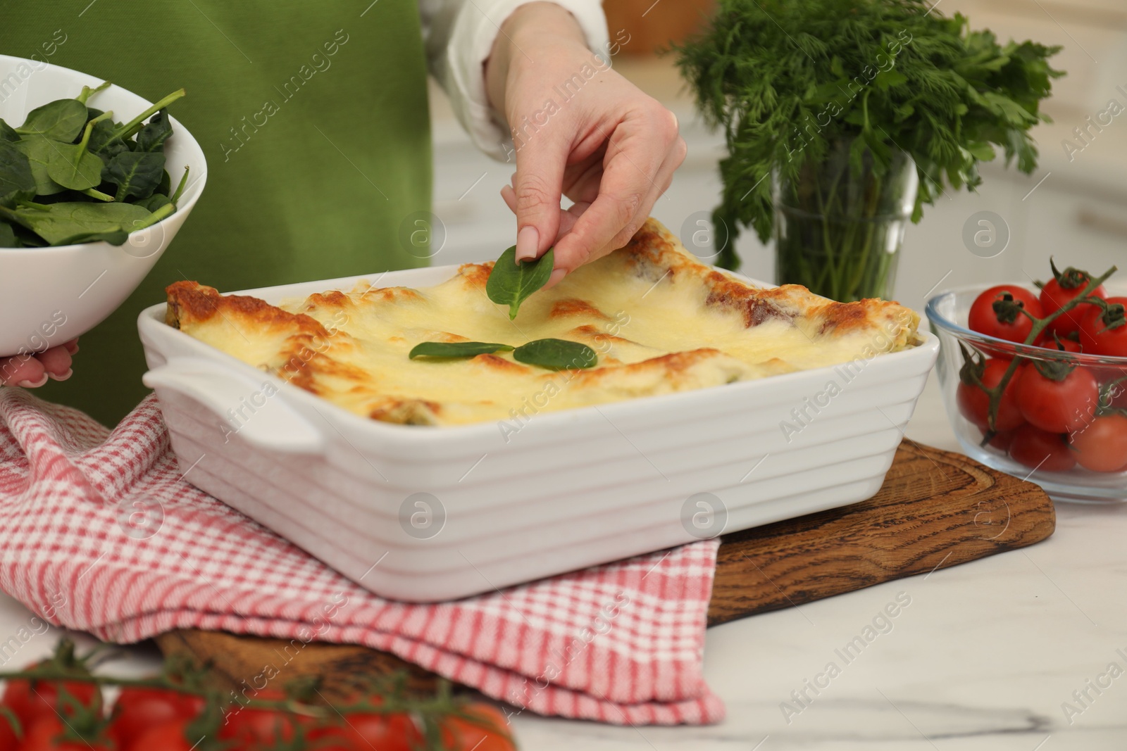 Photo of Woman putting spinach onto lasagna at white table indoors, closeup