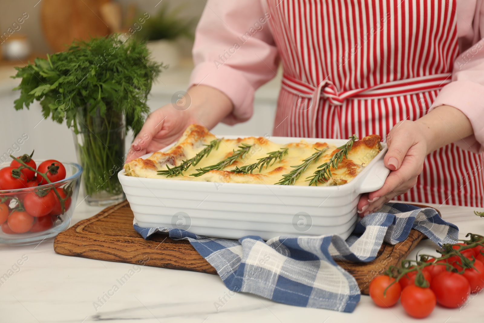 Photo of Woman putting baking dish with tasty lasagna onto white marble table indoors, closeup