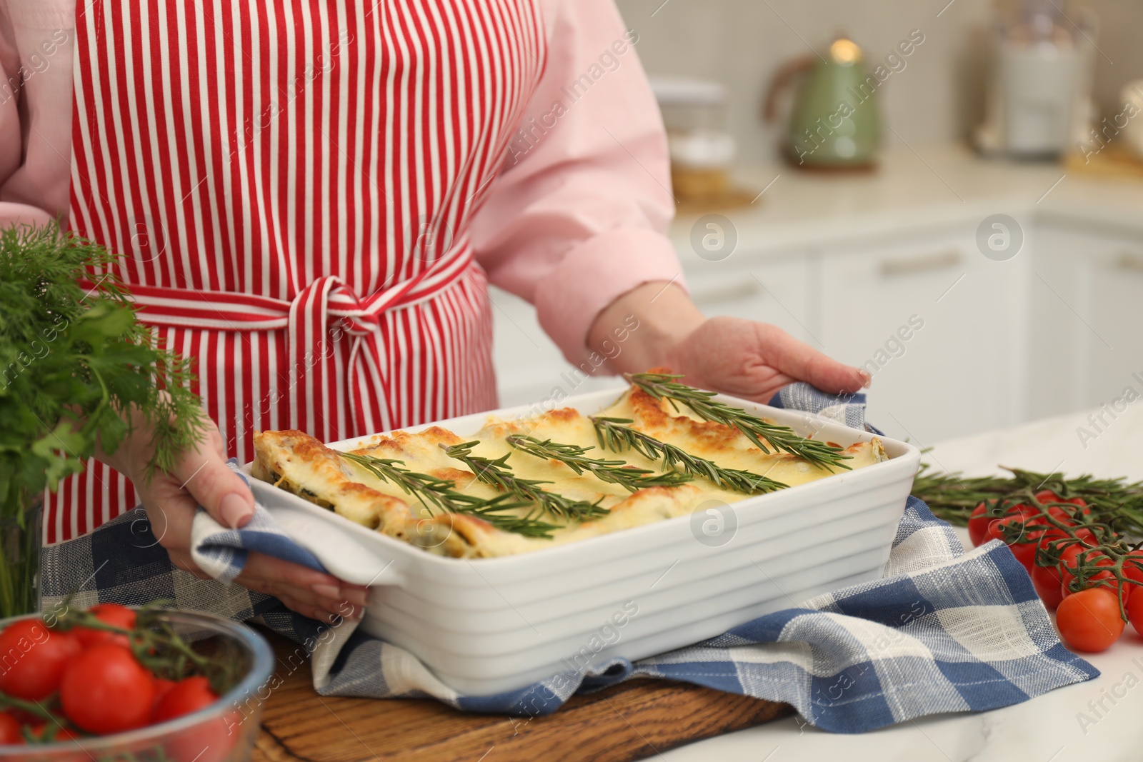 Photo of Woman putting baking dish with tasty lasagna onto white table indoors, closeup