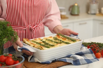 Photo of Woman putting baking dish with tasty lasagna onto white table indoors, closeup