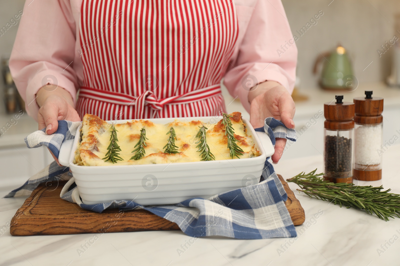 Photo of Woman putting baking dish with tasty lasagna onto white marble table indoors, closeup