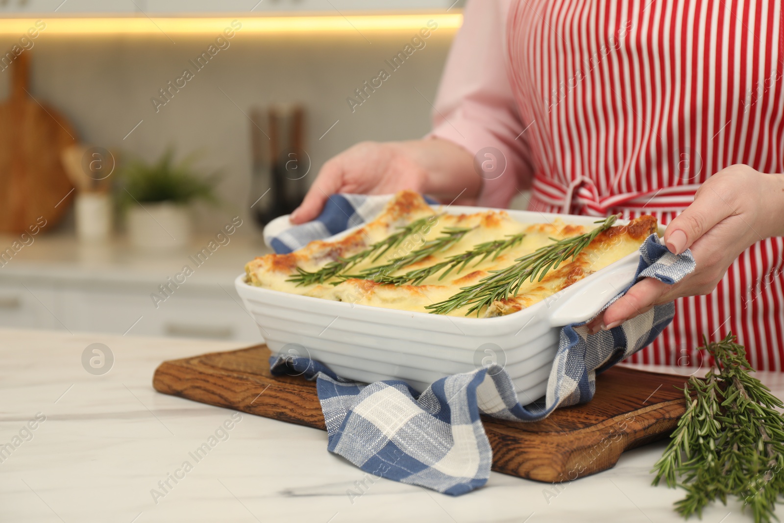 Photo of Woman putting baking dish with tasty lasagna onto white marble table indoors, closeup. Space for text